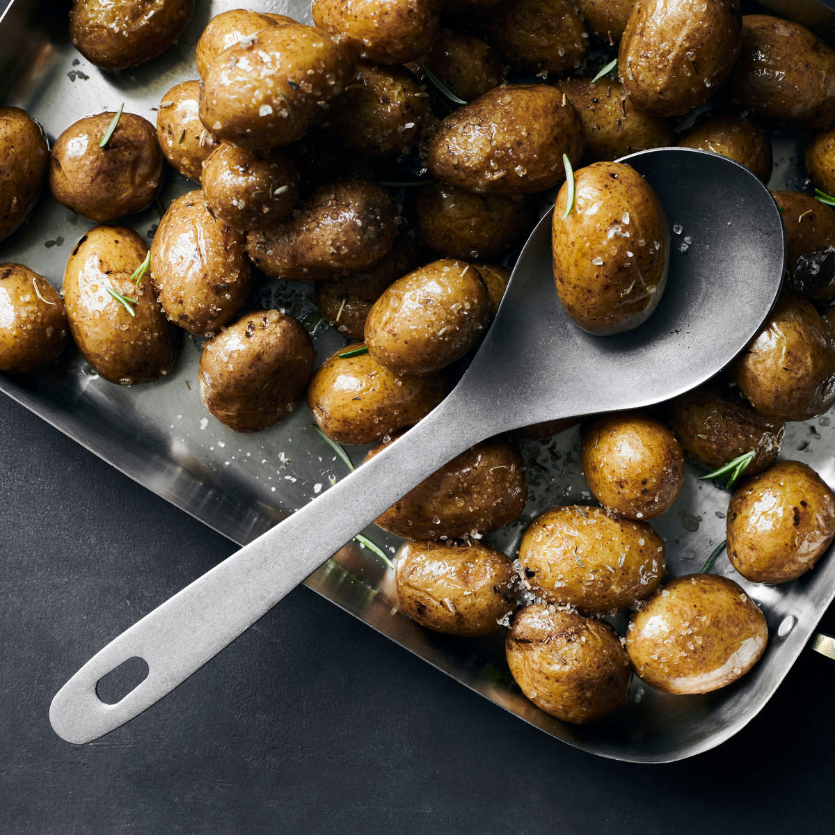 A stainless steel serving spoon, rounded with a long handle and a hole in the end of the handle to hang up the spoon on a hook.