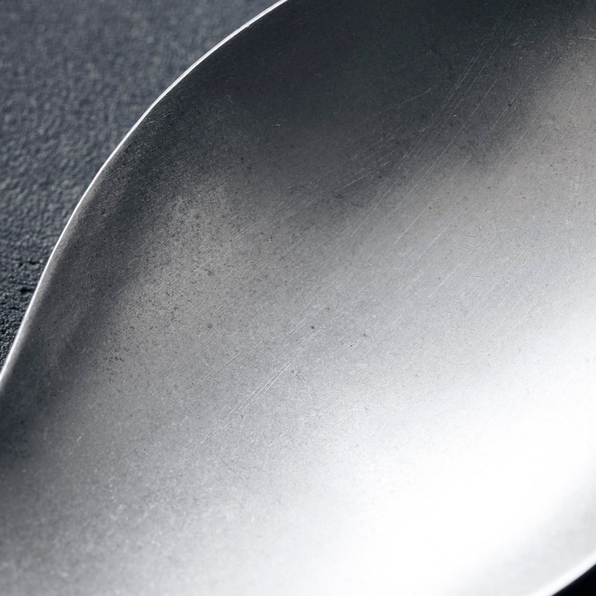 A stainless steel serving spoon, rounded with a long handle and a hole in the end of the handle to hang up the spoon on a hook.