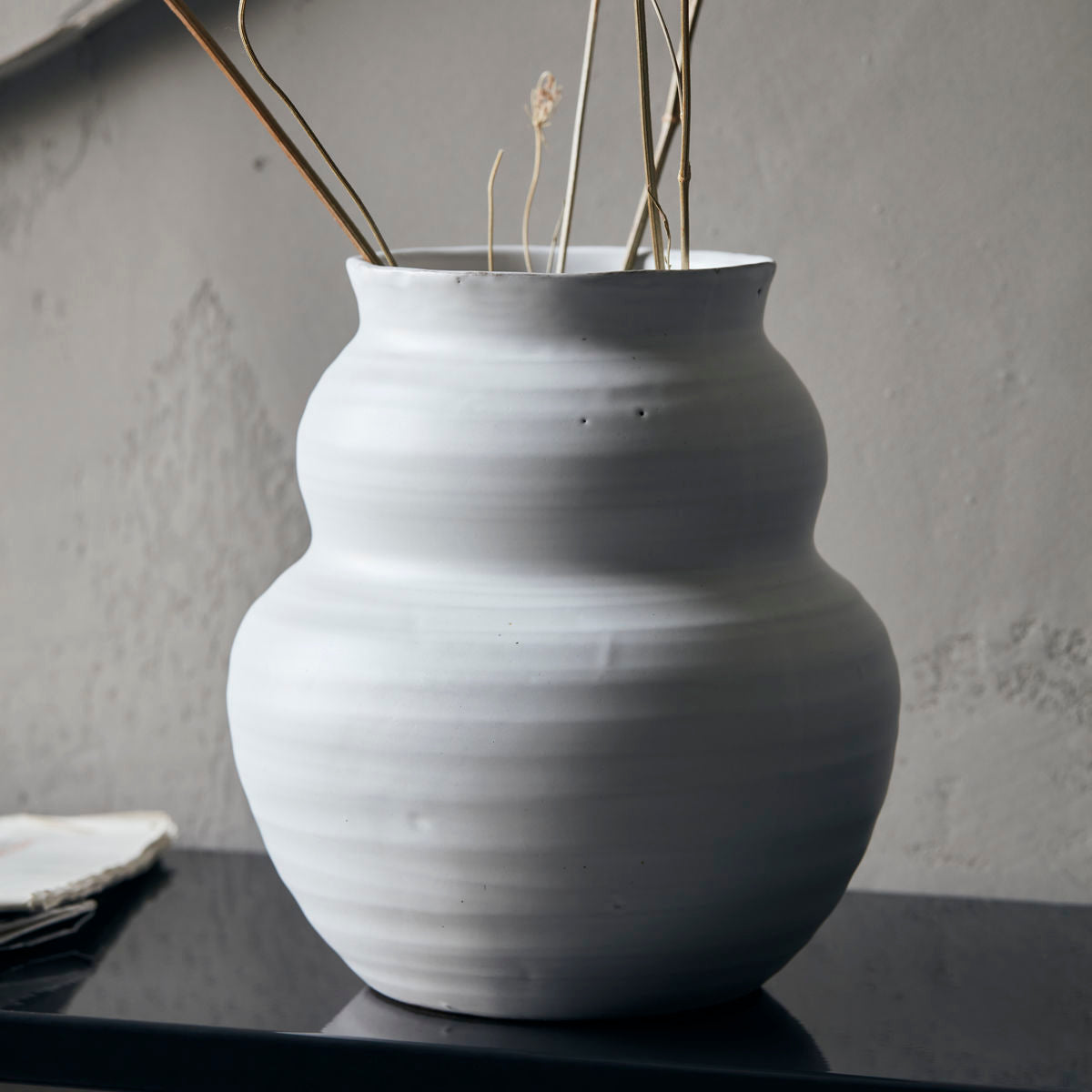 A clay vase glazed in white, with a larger circular base and smaller version of the same shape on top.