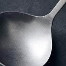 A steel soup ladle with a hole at the top of the handle to hang it up.