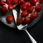 A stainless steel cake server with a hole in the top of the handle for hanging up after use.