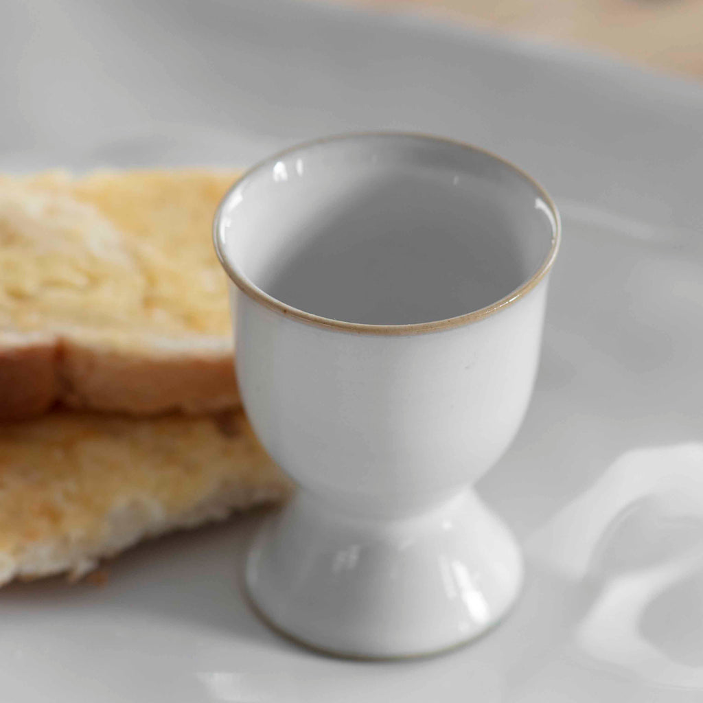 Two white ceramic egg cups with a straw coloured thin band around the top and base.