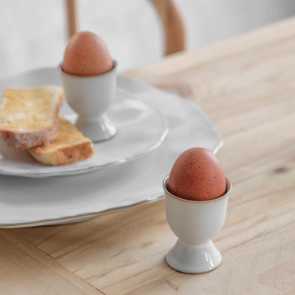 Two white ceramic egg cups with a straw coloured thin band around the top and base.